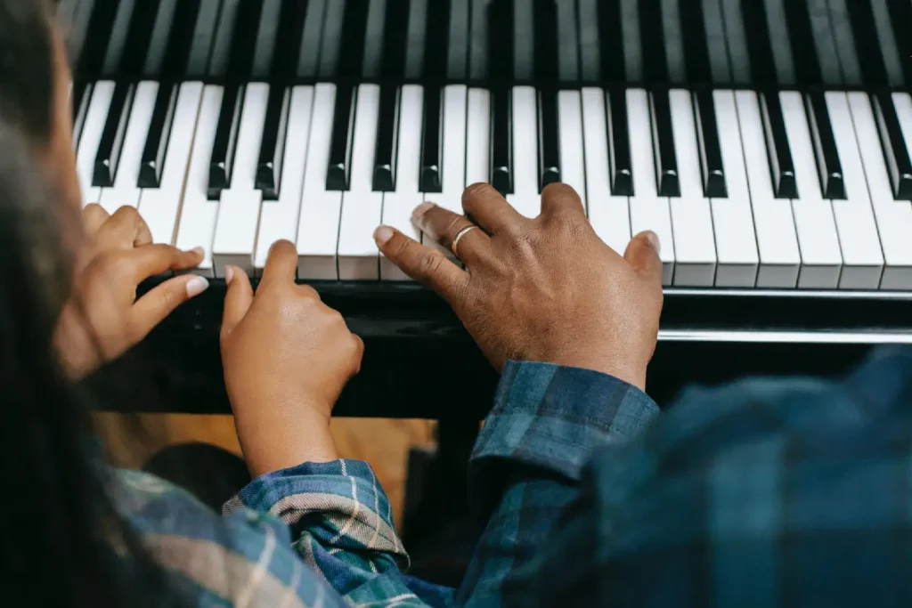 Photo of two people playing the piano, closeup on the keys and hands. Fractional pedaling.