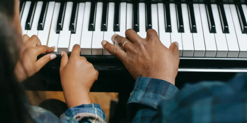Photo of two people playing the piano, closeup on the keys and hands