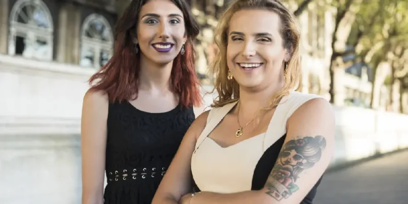 Two transgender women standing together, looking at the camera and smiling