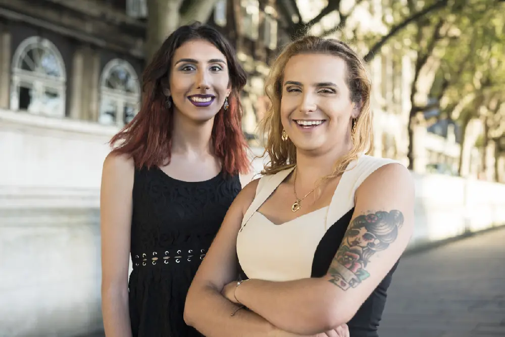 Two transgender women standing together, looking at the camera and smiling