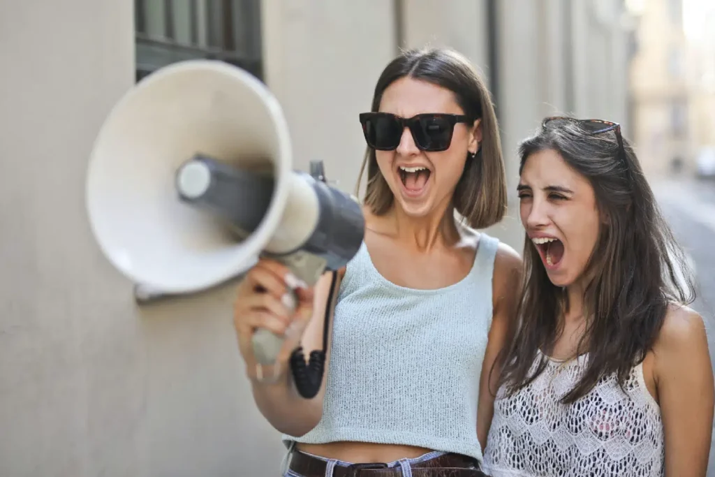 Photo of two people yelling into a megaphone, blurry background of a road