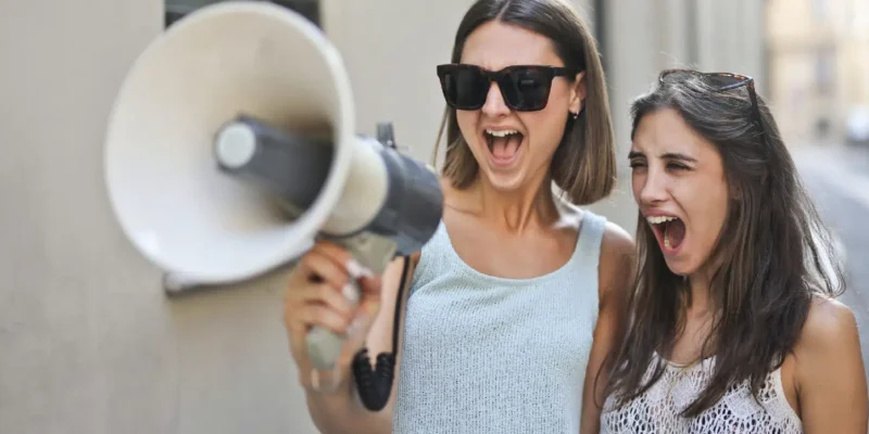 Photo of two people yelling into a megaphone, blurry background of a road