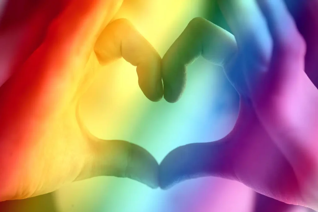 Photo of hands in the shape of a heart, with a rainbow colored overlay
