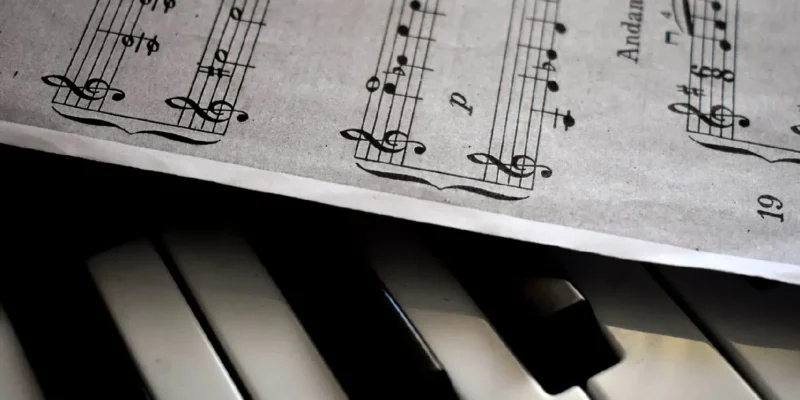 Closeup photo of piano keys with a sheet of a music score over it